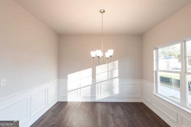 unfurnished dining area featuring an inviting chandelier, a decorative wall, dark wood-type flooring, and wainscoting