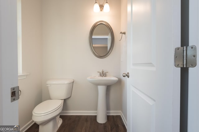 half bath with baseboards, toilet, and wood finished floors