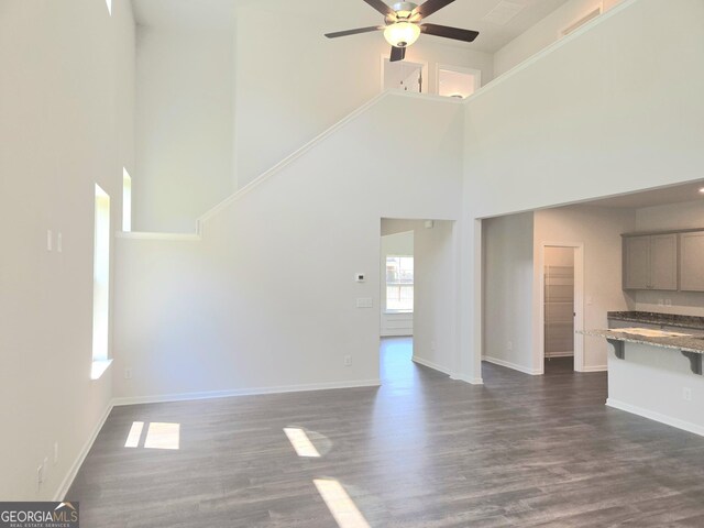 unfurnished living room featuring dark wood-style flooring, ceiling fan, and baseboards