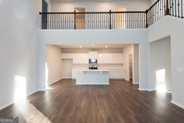 unfurnished living room featuring dark wood-type flooring, a high ceiling, and baseboards