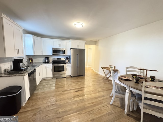 kitchen featuring light wood-style flooring, dark stone countertops, stainless steel appliances, white cabinetry, and a sink