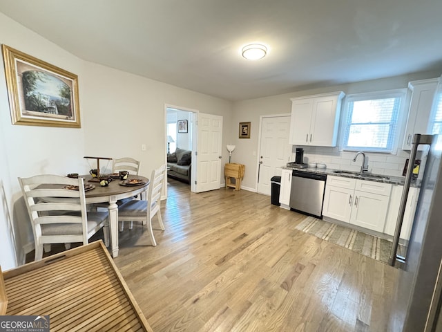 kitchen with white cabinets, dishwasher, light wood-style flooring, backsplash, and a sink