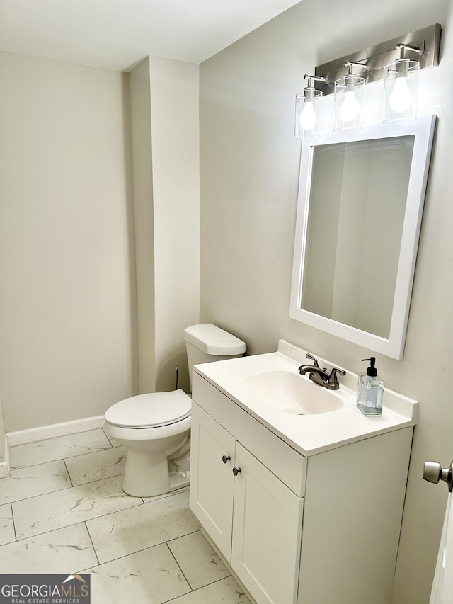 bathroom with toilet, marble finish floor, vanity, and baseboards