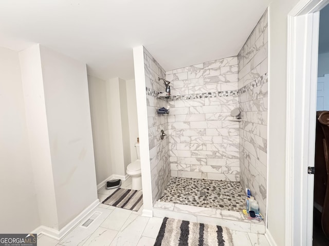 bathroom featuring toilet, baseboards, visible vents, and a tile shower