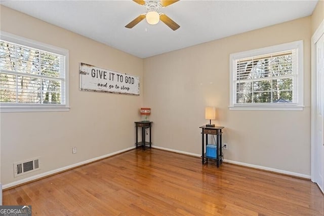 empty room featuring light wood finished floors, baseboards, visible vents, and a wealth of natural light