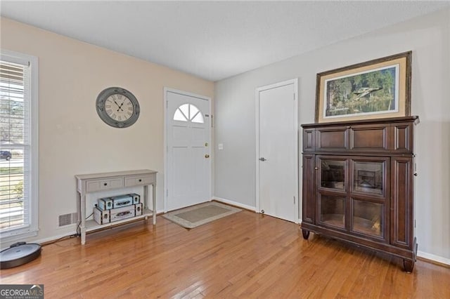 entryway featuring baseboards, wood finished floors, visible vents, and a healthy amount of sunlight