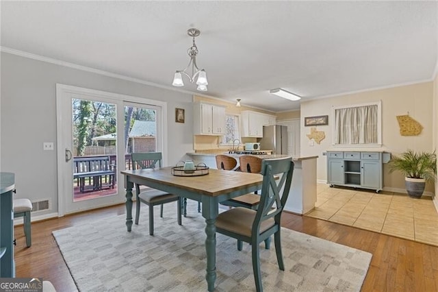 dining space with ornamental molding, light wood-type flooring, visible vents, and baseboards