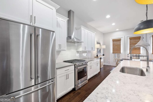 kitchen featuring white cabinets, wall chimney range hood, high end appliances, and a sink