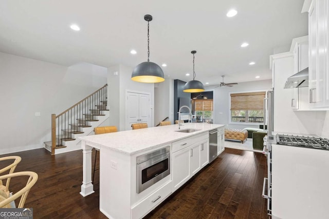 kitchen featuring a breakfast bar area, under cabinet range hood, a sink, appliances with stainless steel finishes, and a center island with sink