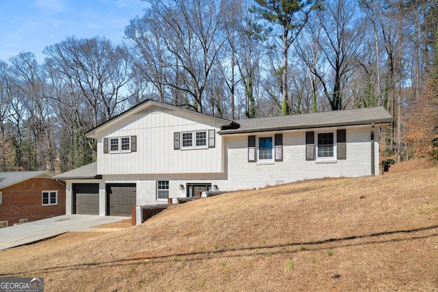 tri-level home featuring a garage, concrete driveway, brick siding, and a front lawn