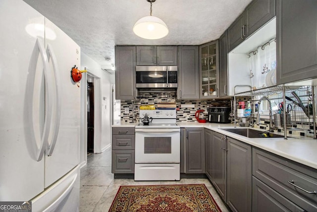 kitchen with white appliances, a sink, backsplash, gray cabinets, and glass insert cabinets