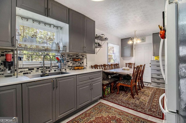 kitchen with decorative backsplash, freestanding refrigerator, light countertops, gray cabinetry, and a sink