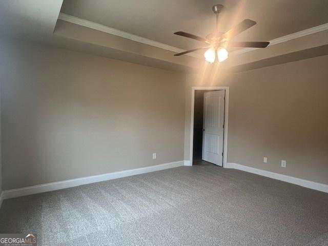 spare room featuring baseboards, a raised ceiling, ceiling fan, ornamental molding, and carpet floors