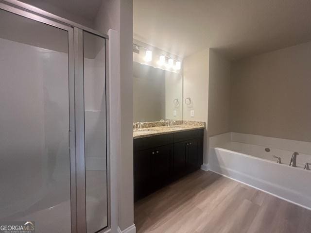 full bath featuring a stall shower, double vanity, a garden tub, and wood finished floors