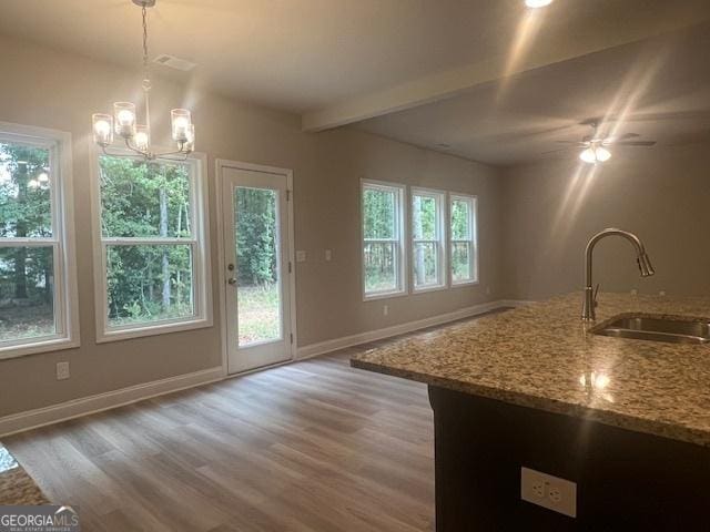 kitchen featuring light stone counters, beamed ceiling, light wood-style floors, pendant lighting, and a sink