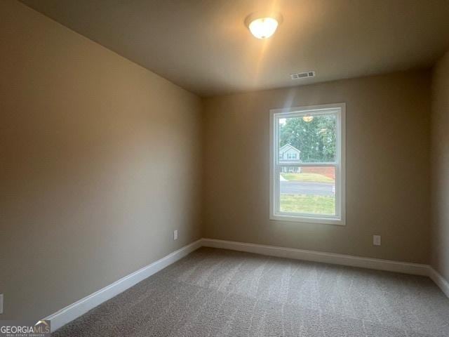 empty room with carpet, visible vents, and baseboards