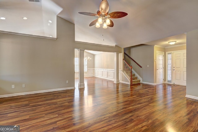 unfurnished living room with ceiling fan with notable chandelier, dark wood-style flooring, ornamental molding, stairway, and decorative columns