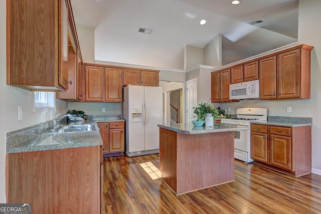 kitchen with white appliances, visible vents, a kitchen island, light stone countertops, and a sink