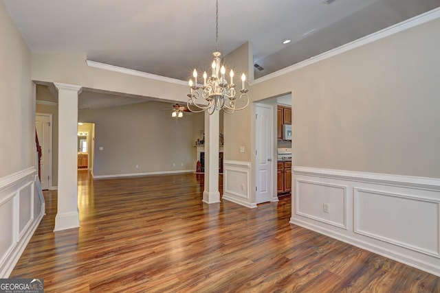 unfurnished dining area featuring dark wood-style flooring, a decorative wall, ornamental molding, ornate columns, and ceiling fan with notable chandelier