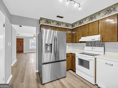 kitchen with light wood-type flooring, white appliances, light countertops, and under cabinet range hood