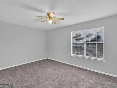 spare room with carpet floors, ceiling fan, a textured ceiling, and baseboards