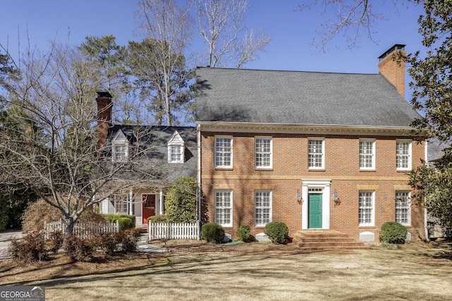 colonial-style house featuring brick siding, a chimney, and fence