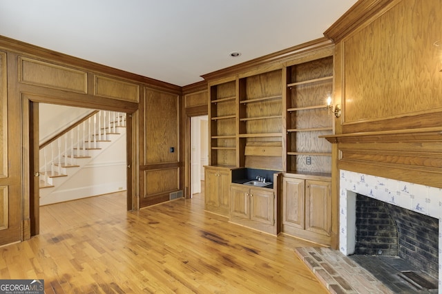 unfurnished living room featuring ornamental molding, light wood-type flooring, stairs, and a premium fireplace