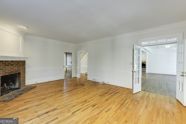 unfurnished living room featuring french doors, light wood finished floors, visible vents, ornamental molding, and a brick fireplace