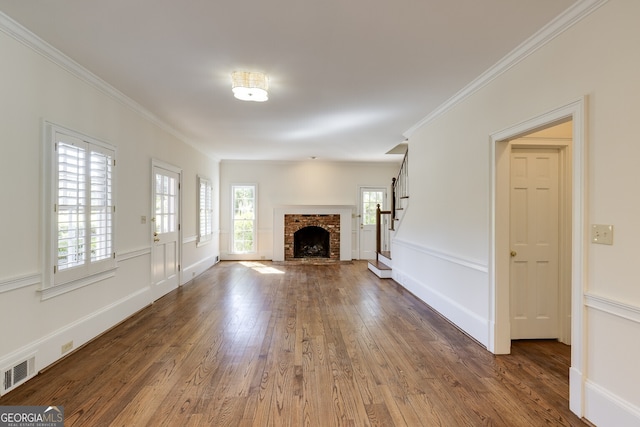 unfurnished living room featuring crown molding, visible vents, a brick fireplace, wood finished floors, and stairs