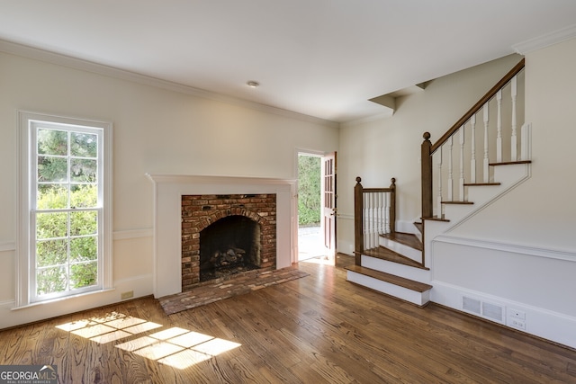 unfurnished living room featuring a healthy amount of sunlight, crown molding, stairs, and wood finished floors