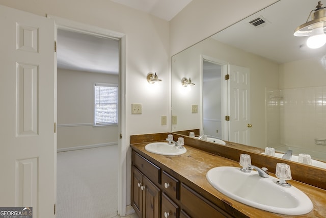 bathroom featuring double vanity, visible vents, a tile shower, and a sink