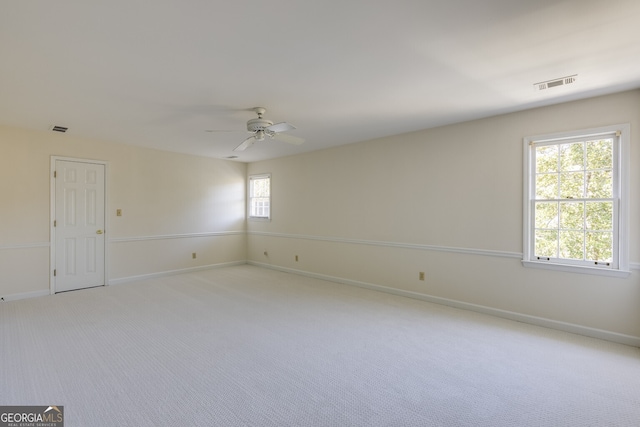 spare room with light carpet, ceiling fan, visible vents, and baseboards