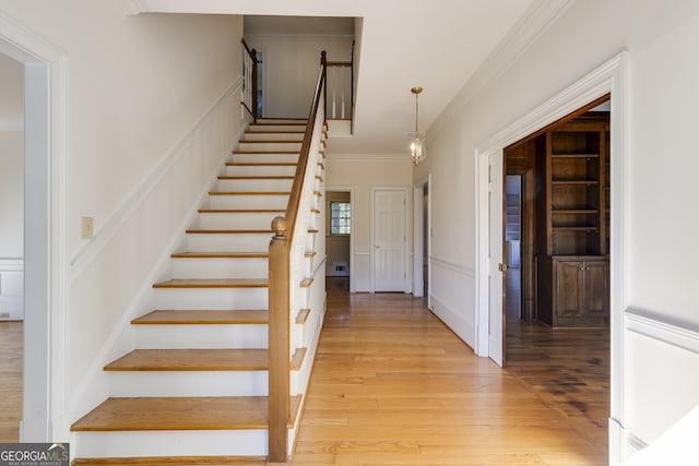 stairway featuring a wainscoted wall, ornamental molding, wood finished floors, built in shelves, and a decorative wall