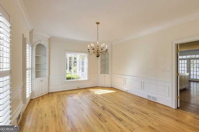 unfurnished dining area featuring built in shelves, visible vents, ornamental molding, a chandelier, and light wood-type flooring