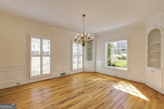 unfurnished dining area with built in features, light wood-type flooring, a chandelier, and visible vents