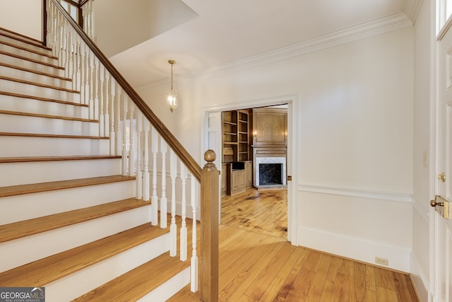 staircase featuring built in features, baseboards, ornamental molding, wood finished floors, and a fireplace