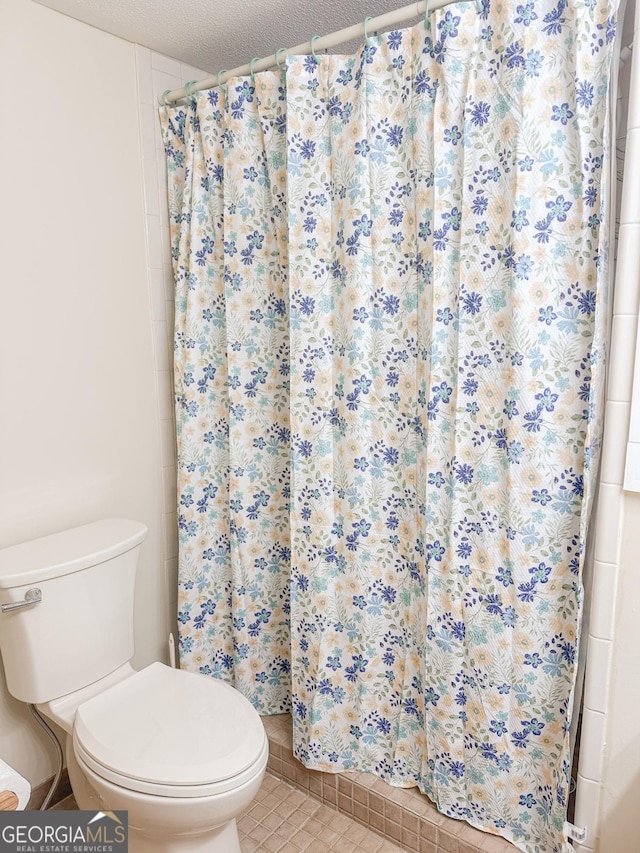 bathroom featuring a shower stall, a textured ceiling, toilet, and tile patterned floors