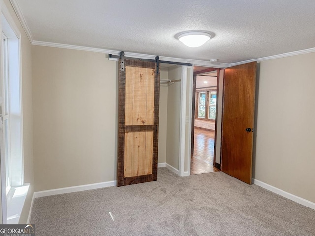 unfurnished bedroom featuring carpet floors, a barn door, a textured ceiling, and crown molding