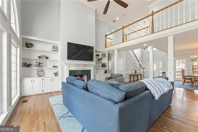 living area featuring built in features, a fireplace, crown molding, light wood-type flooring, and ornate columns