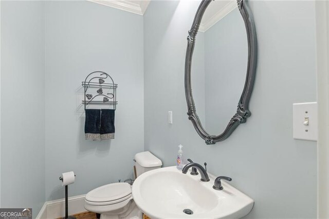 half bathroom featuring toilet, baseboards, a sink, and ornamental molding