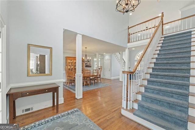 entrance foyer featuring a high ceiling, wood finished floors, visible vents, stairs, and an inviting chandelier