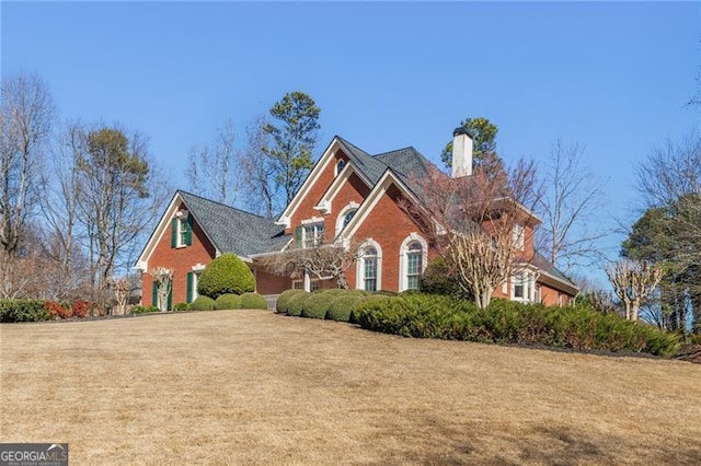 view of front of property with brick siding, a chimney, and a front yard