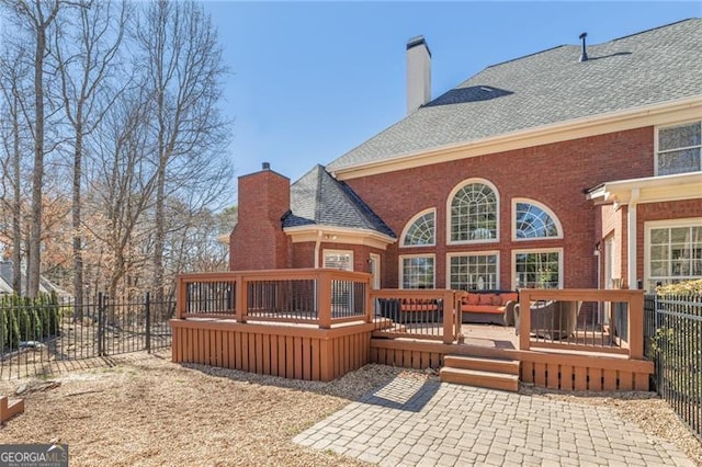 rear view of house with brick siding, fence, a chimney, and a wooden deck