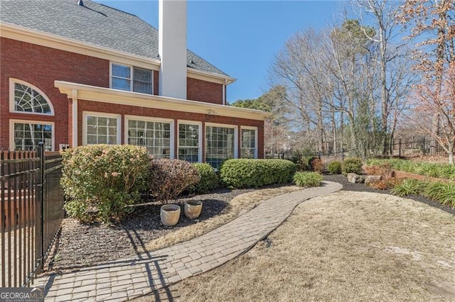 rear view of property with roof with shingles, brick siding, a chimney, and fence