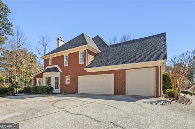 colonial house featuring brick siding, driveway, a chimney, and an attached garage