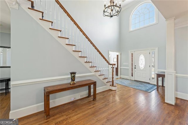 entryway with ornamental molding, decorative columns, stairway, and wood finished floors