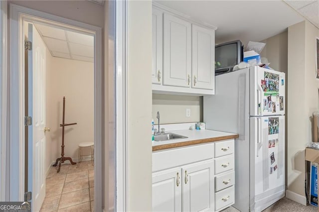 kitchen featuring light tile patterned floors, light countertops, freestanding refrigerator, white cabinets, and a sink