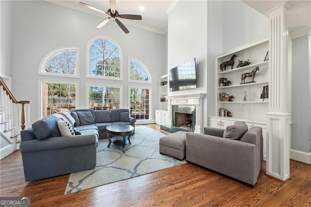 living room with a towering ceiling, a premium fireplace, stairway, wood finished floors, and crown molding