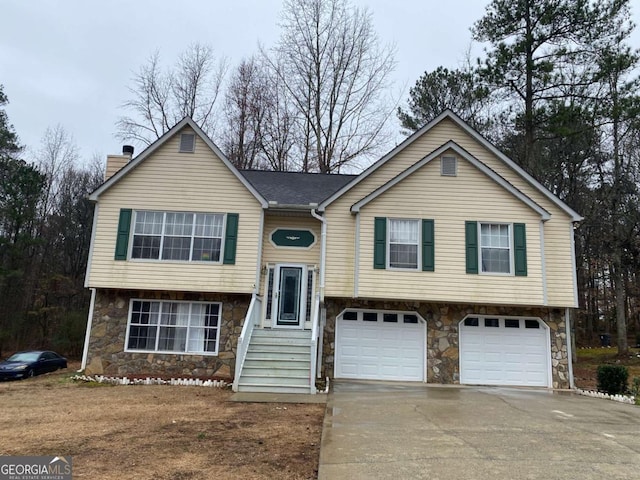 bi-level home with stone siding, an attached garage, a chimney, and concrete driveway