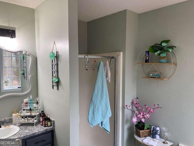 full bath with a shower with shower door, a textured ceiling, and vanity